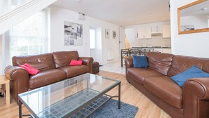 A modern living room with two brown leather sofas, a glass coffee table, and a staircase leading to another level. - Inglenook House, Holiday Home Manorbier, Sleeps 8, 4 bedrooms,  bathrooms (TENBY)
