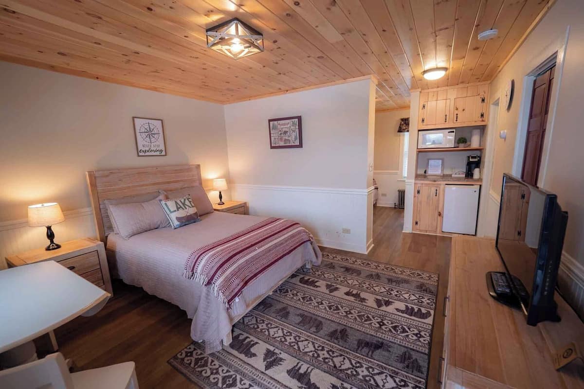 Een knus slaapkamer met een houten plafond, een bed met een geborduurde deken, een nachtkastje en een klein bureau.