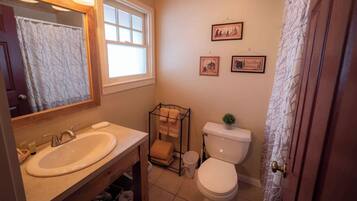 A bathroom with a sink, mirror, window, toilet, and two framed pictures on the wall.