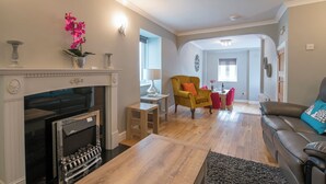 A living room with a fireplace, a sofa, a coffee table, and a dining area with a yellow armchair and red chairs. - Inkerman House, Holiday Cottage Saundersfoot, Sleeps 4, 2 bedrooms,  bathrooms (Saundersfoot)