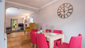 A dining area with a wooden table, red chairs, a large wall clock, and a television in the background. - Inkerman House, Holiday Cottage Saundersfoot, Sleeps 4, 2 bedrooms,  bathrooms (Saundersfoot)