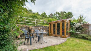 A patio with two chairs and a table, a wooden structure with glass doors, and a stone wall. - Ivy Cottage, Holiday Cottage Little Haven, Sleeps 5, 2 bedrooms,  bathrooms (Haverfordwest)