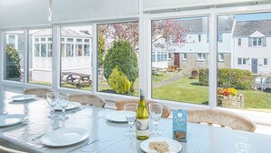 A dining table set for four with a bottle of wine and a menu, overlooking a garden with houses. - Ivy Tower House, Holiday Home Ivy Tower Village, St Florence, Sleeps 12, 6 bedrooms,  bathrooms (Tenby)