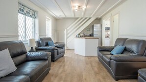 A modern living room with two leather sofas, a wooden floor, and a kitchen area in the background. - Ivy Tower House, Holiday Home Ivy Tower Village, St Florence, Sleeps 12, 6 bedrooms,  bathrooms (Tenby)