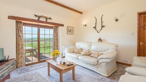 A cozy living room with a white leather sofa, a wooden coffee table, and a view through a large glass door to the outdoors. - Kingfisher Cottage, Holiday Cottage St Ishmaels, Near Dale, Sleeps 4, 2 bedrooms,  bathrooms (Haverfordwest)