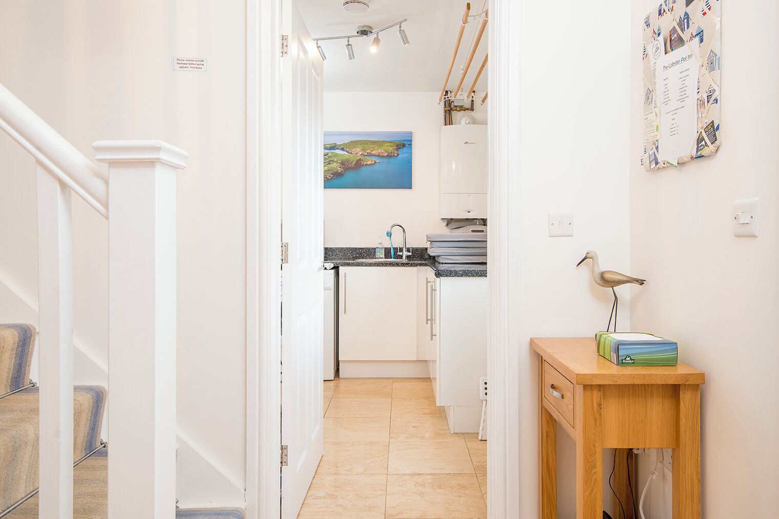 A hallway leading to a kitchen with a view of the sea, a wooden table with a lamp, and a wall-mounted calendar.