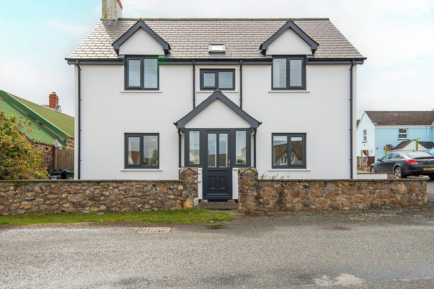 A two-story house with a stone foundation, a central entrance with a black door, and multiple windows with dark frames.