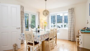 Un comedor con una mesa preparada para dos personas, sillas, una lámpara colgante y vistas a través de las ventanas.