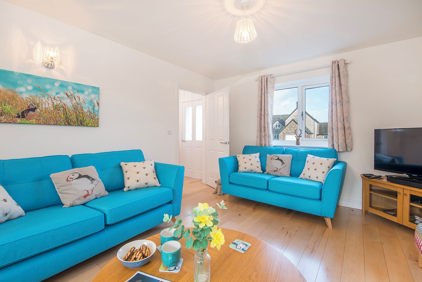 A bright living room with two blue sofas, a wooden coffee table, and a TV stand.