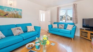 Un salón luminoso con dos sofás azules, una mesa de centro de madera y un mueble para la televisión.