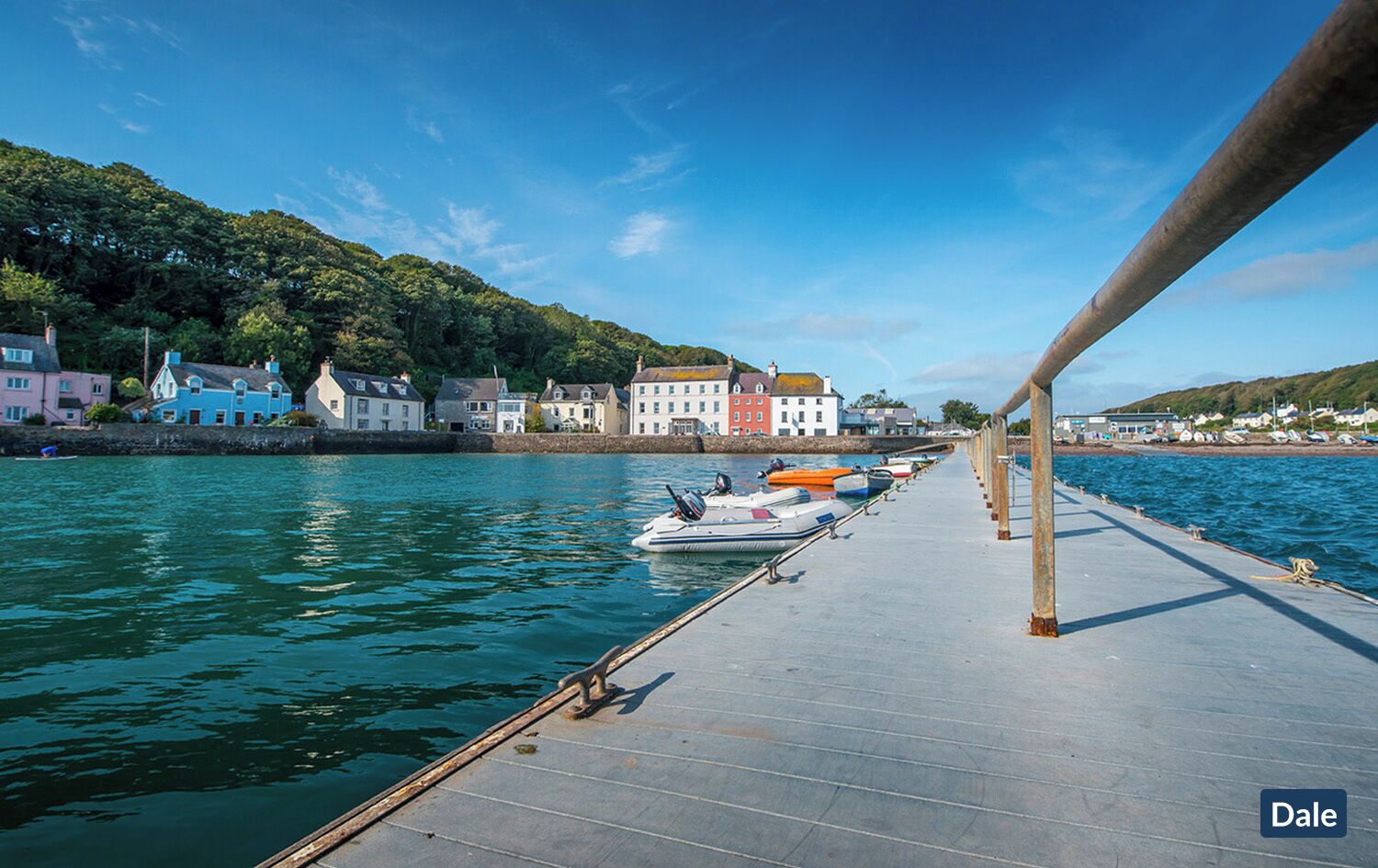 A pier with boats docked, a stone wall, and colorful buildings along the water.