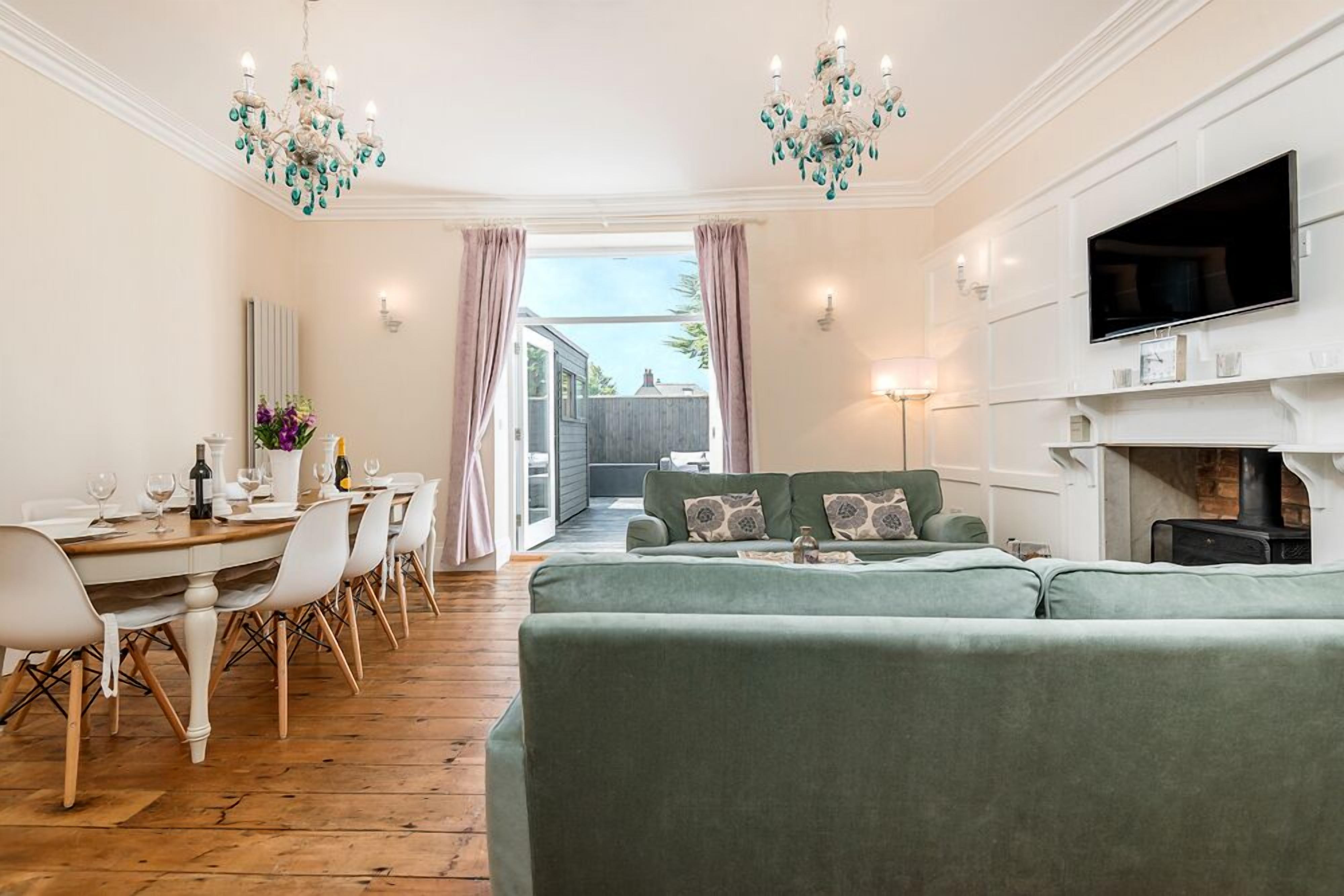 A living room with a green sofa, a dining table with chairs, and a TV mounted on the wall.