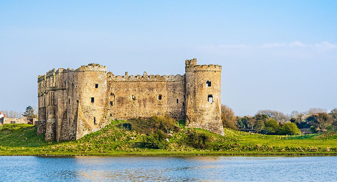 Un château historique, doté de douves, entouré de verdure et surplombé d’un ciel dégagé.