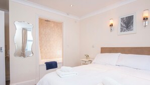 A hotel room with a large bed, a bathroom with a shower, a mirror, and two wall-mounted lights. - Lantern Suite, Holiday Apartment Tenby, Pembrokeshire, Sleeps 2, 1 bedrooms,  bathrooms (Tenby)