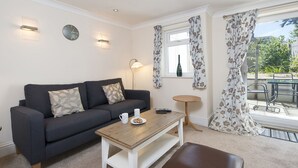 A living room with a dark grey sofa, a wooden coffee table, a brown leather ottoman, and a small round side table. - Lantern Suite, Holiday Apartment Tenby, Pembrokeshire, Sleeps 2, 1 bedrooms,  bathrooms (Tenby)