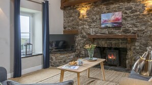 A cozy living room with a stone fireplace, a television, and a table with a vase of flowers. - Little Folly, Holiday Cottage Nolton Haven, Sleeps 4, 2 bedrooms,  bathrooms (Haverfordwest)