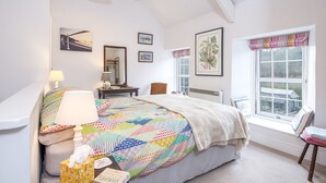 A bedroom with a large bed, a bedside table, a chair, a window with a view, and a mirror on the wall.
