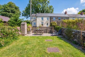A two-story house with a stone facade, a wooden fence, and a grassy backyard with a bench and a chair. - Llanmill Cottage, holiday home Llanmill, Nr Narberth, Sleeps 2, 1 bedrooms,  bathrooms (Nr Narberth)