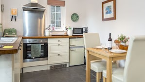 A compact kitchen with a stove, oven, microwave, and a small refrigerator. There is a dining table with chairs and a single wine bottle.