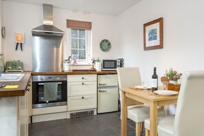 A compact kitchen with a stove, oven, microwave, and a small refrigerator. There is a dining table with chairs and a single wine bottle.