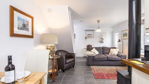 A modern living room with a fireplace, a dining area with a bottle of wine, and a sofa with cushions.