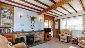 A cozy living room with a stone fireplace, wooden beams, a television, leather armchairs, and a bookshelf filled with books and decorative items. - Llanwg, Holiday Cottage Trefin, Sleeps 5, 3 bedrooms,  bathrooms (Trefin)