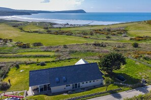 Une maison située sur la côte, avec vue sur la mer, entourée de champs verdoyants et d’un petit jardin.