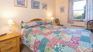 A bedroom with a bed, bedside lamps, a wooden nightstand, a chair, and a window with curtains. - Lower Coach House, Holiday Home Fishguard, Sleeps 2, 1 bedrooms,  bathrooms (Fishguard)
