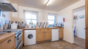 A kitchen with a stove, oven, washing machine, and dishwasher. There are windows, a clock, and a fire extinguisher. - Lower Coach House, Holiday Home Fishguard, Sleeps 2, 1 bedrooms,  bathrooms (Fishguard)