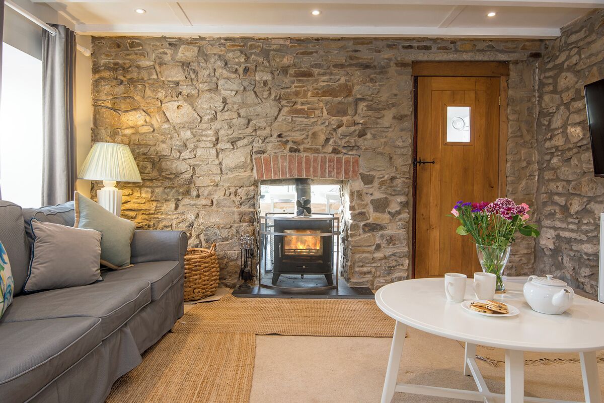 A cozy living room with a stone wall, a fireplace, a sofa, a table with cups and a vase of flowers.