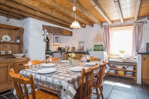 Une cuisine rustique avec des meubles de rangement en bois, une table à manger pour quatre personnes et une fenêtre agrémentée de rideaux.