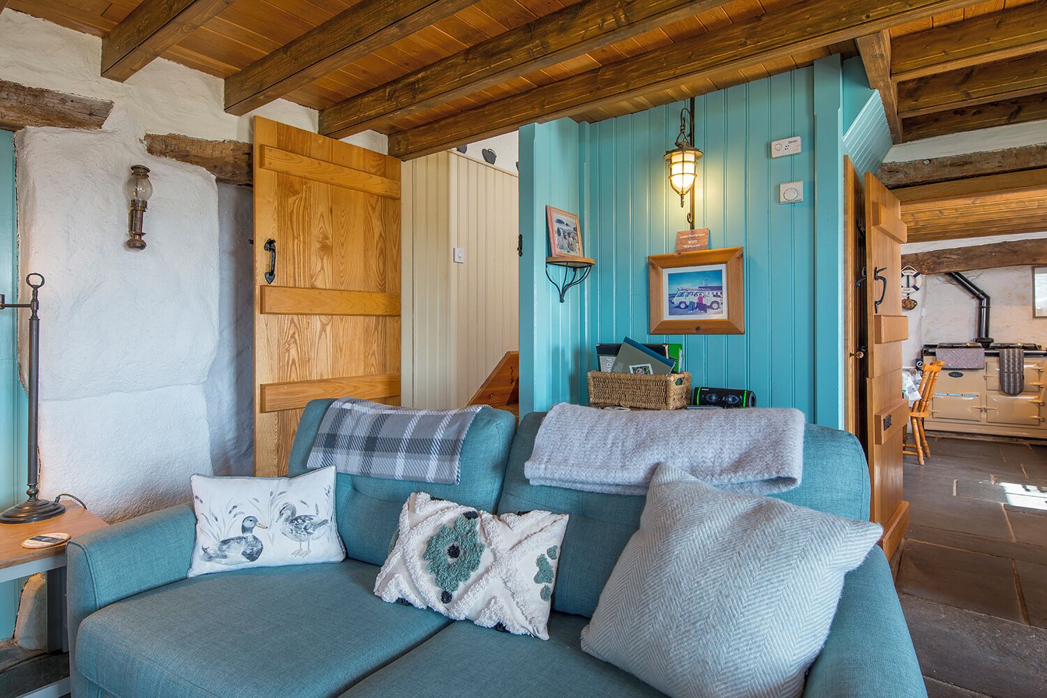 A cozy room with a blue sofa, a wooden door, a wall-mounted lamp, and a framed picture.