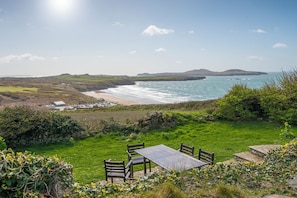 A coastal landscape with a grassy area, a stone wall, and a table with chairs.
