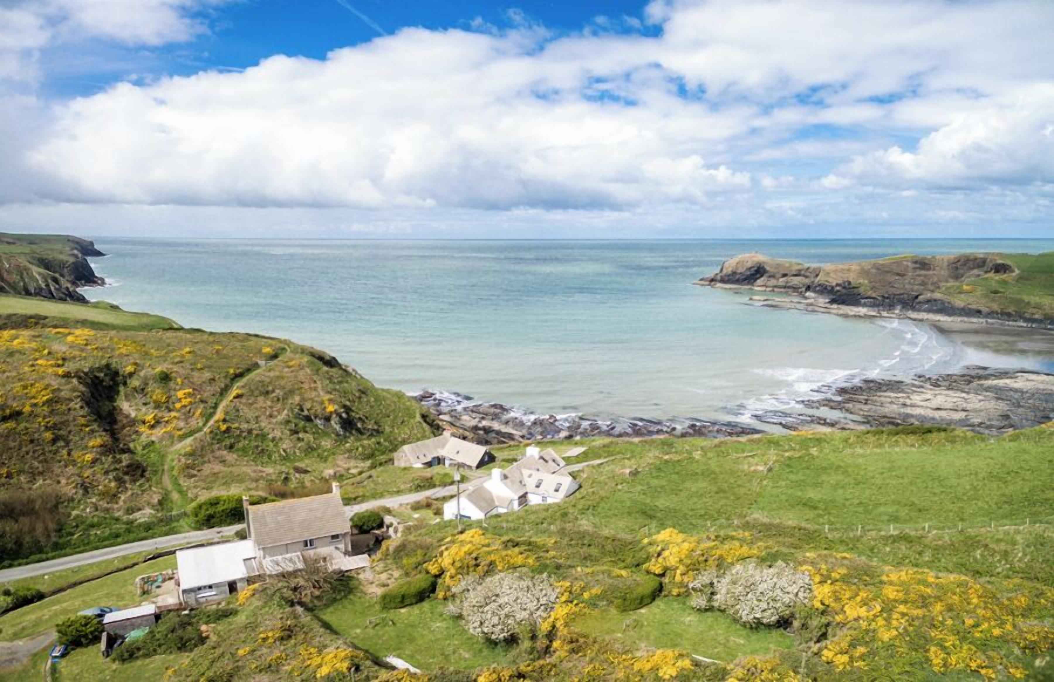 A coastal village with houses near the sea, a road, and grassy hills.
