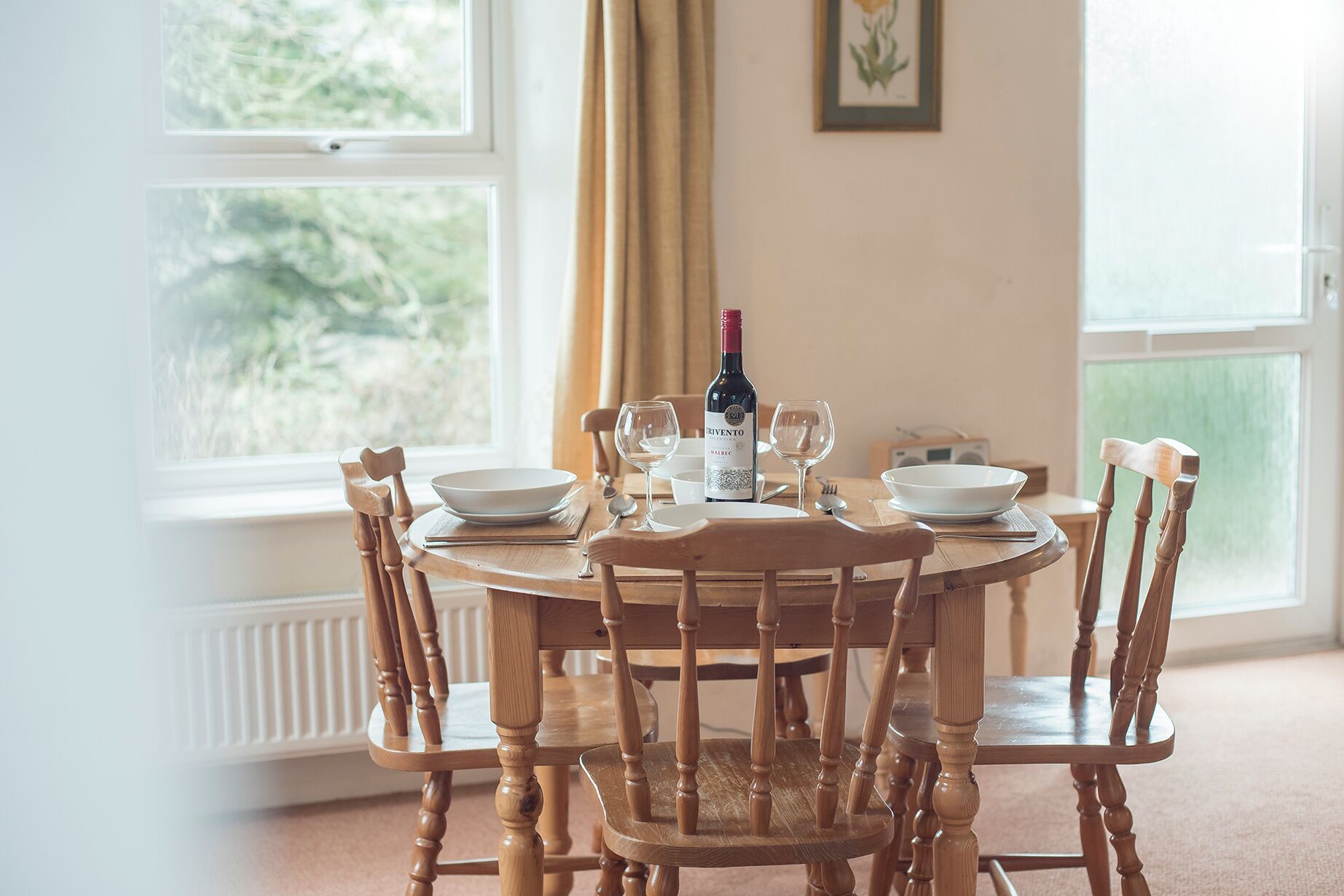 A dining table set with white plates, wine glasses, and a bottle of wine.