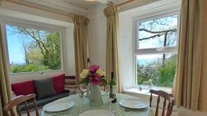 A dining area with a round table set for four, a vase of flowers, and a bottle of wine. - Middle Hill Cottage, Holiday Cottage Amroth, Sleeps 4, 2 bedrooms,  bathrooms (Amroth)