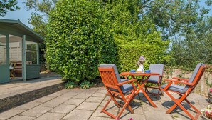 A patio with a table and four chairs, a small shed, and a large bush. - Minim Cottage, Holiday Cottage Saundersfoot, Sleeps 4, 2 bedrooms,  bathrooms (Saundersfoot)