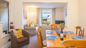 A dining area with a wooden table set for two, a sofa with cushions, and a window with curtains. - Minim Cottage, Holiday Cottage Saundersfoot, Sleeps 4, 2 bedrooms,  bathrooms (Saundersfoot)