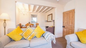 A cozy living room with a sofa set, a dining table, and a wooden door. - Minim Cottage, Holiday Cottage Saundersfoot, Sleeps 4, 2 bedrooms,  bathrooms (Saundersfoot)