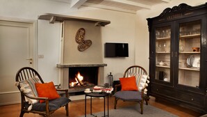 A living room with a fireplace, two armchairs, a coffee table, and a cabinet with glass doors. - Como Lake Panorama apartment Sveva with fireplace and private terrace (Cernobbio)