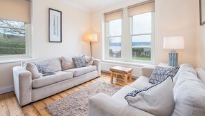 A spacious living room with a beige sofa set, a small wooden stool, and a lamp. - Musselwick House, holiday property St Ishmaels, Near Dale, Sleeps 8, 4 bedrooms,  bathrooms (Haverfordwest)