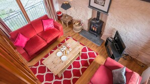 A cozy living room with a red sofa, a wooden coffee table, and a fireplace. - Nolton Coach House, Holiday Cottage Nolton Haven, Sleeps 2, 1 bedrooms,  bathrooms (Haverfordwest)