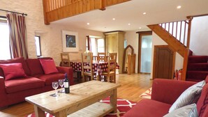 A living room with a red sofa, a wooden table with wine glasses, and a staircase. - Nolton Coach House, Holiday Cottage Nolton Haven, Sleeps 2, 1 bedrooms,  bathrooms (Haverfordwest)