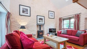 A cozy living room with a fireplace, red sofas, and framed pictures on the wall. - Nolton Coach House, Holiday Cottage Nolton Haven, Sleeps 2, 1 bedrooms,  bathrooms (Haverfordwest)
