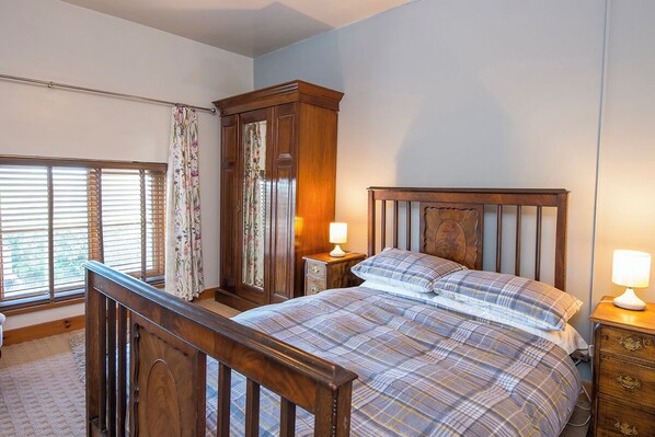 A bedroom with a wooden bed, a nightstand, a dresser, and a window with blinds.