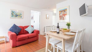 Una sala moderna con un sofá rojo, una mesa de comedor blanca y sillas. Hay una botella de vino y una cesta de fruta sobre la mesa.