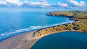 Vista aérea de un paisaje costero con playa, acantilados y colinas ondulantes.