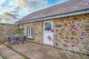 A stone building with a tiled roof, a door, and a window. There is a table and chairs outside. - Picture Cottage, Holiday Home Llanunwas, Solva, Sleeps 2, 1 bedrooms,  bathrooms (Solva)