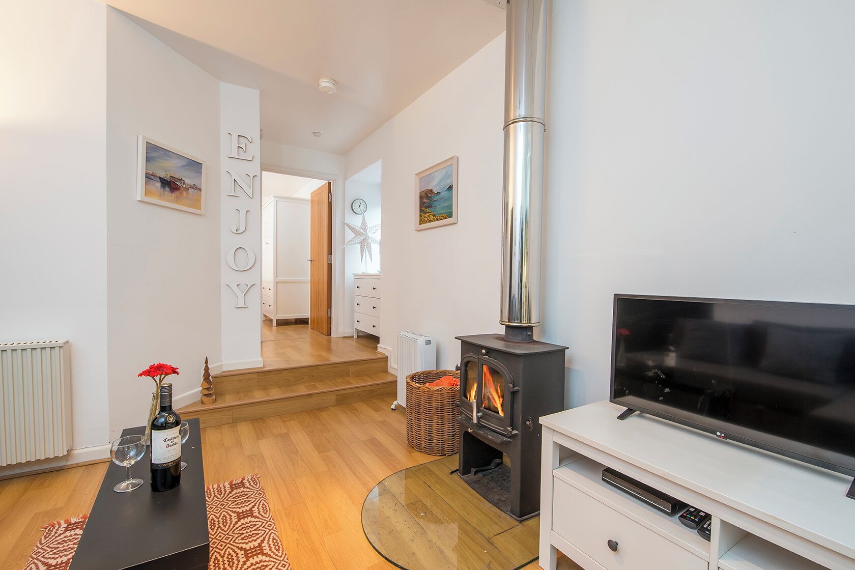 A modern living room with a fireplace, a TV, and a cozy seating area with a rug and a bottle of wine.