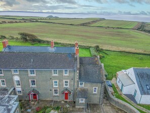 A large building with multiple windows and a red door, surrounded by green fields and a body of water. - Ramsey View, Holiday property Llanunwas, Solva, Sleeps 6, 3 bedrooms,  bathrooms (Solva)